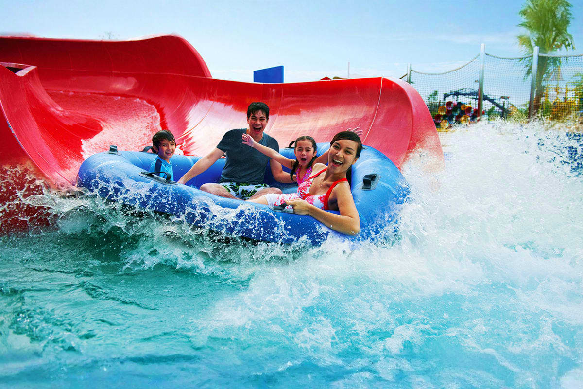 Group of children riding a blue inflatable tube down a red water slide at Legoland Water Park with splashing waves