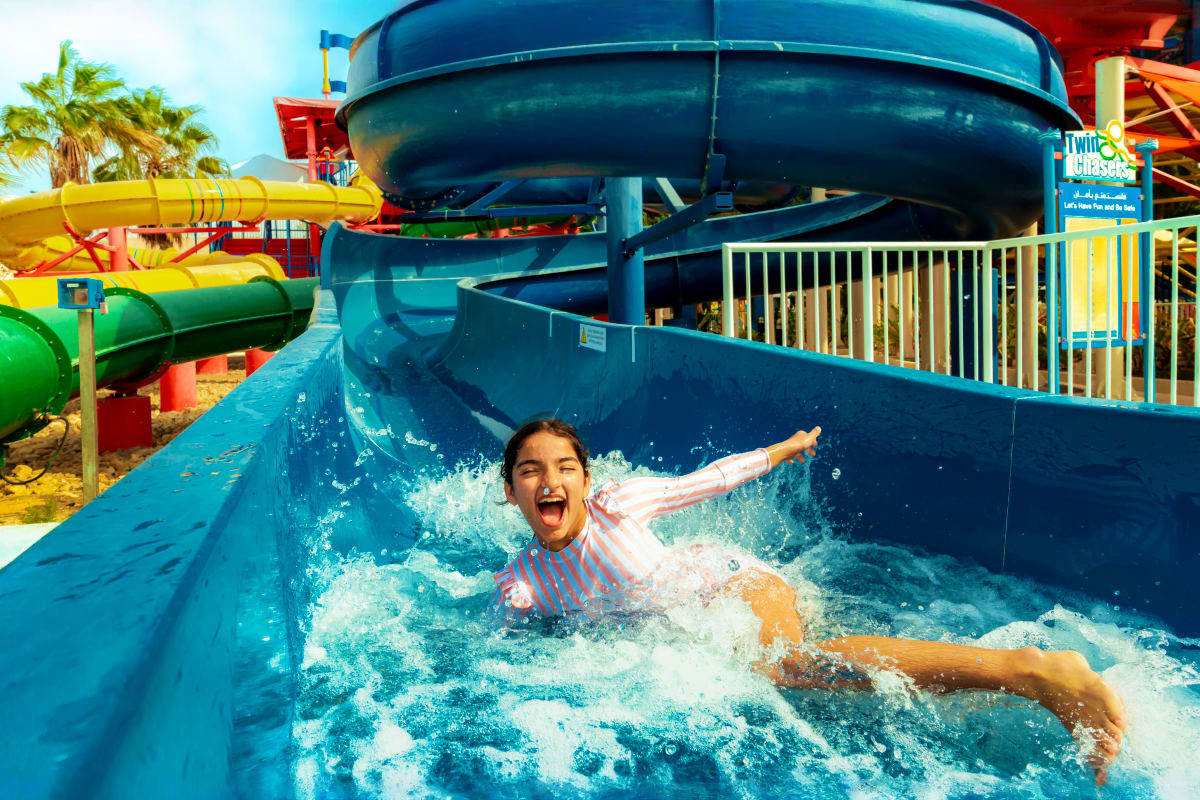 Legoland Water Park Child splashing down blue water slide at Legoland Water Park with colorful slides and palm trees in background