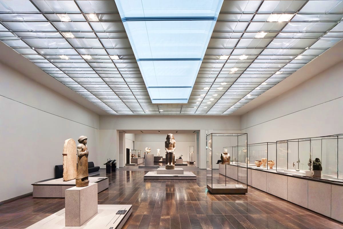 Modern museum gallery with Egyptian statues, glass display cases, and skylights at Louvre Abu Dhabi