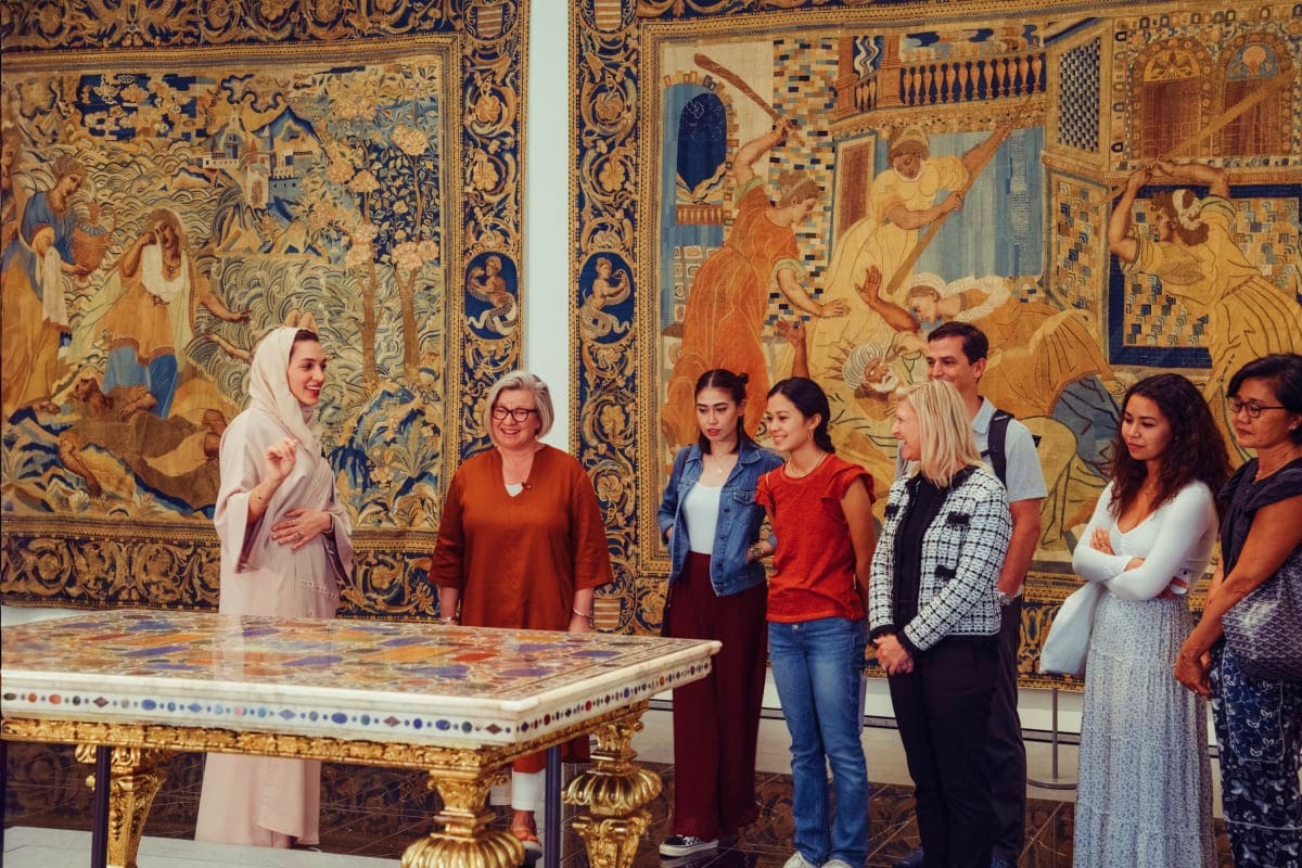 Group of visitors viewing ornate tapestries and decorative table at Louvre Abu Dhabi museum gallery