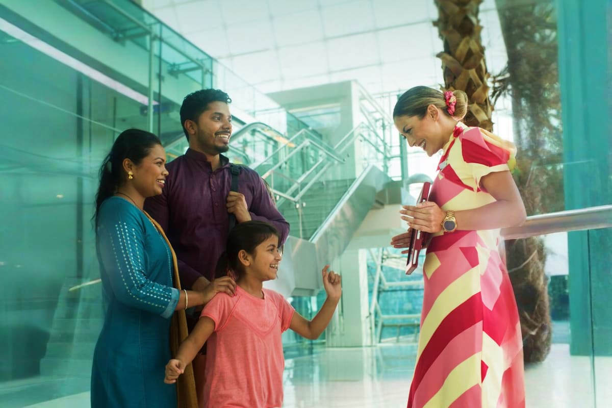 Marhaba Services Dubai Indian family interacting with female staff member in modern glass building with palm tree and staircase in background