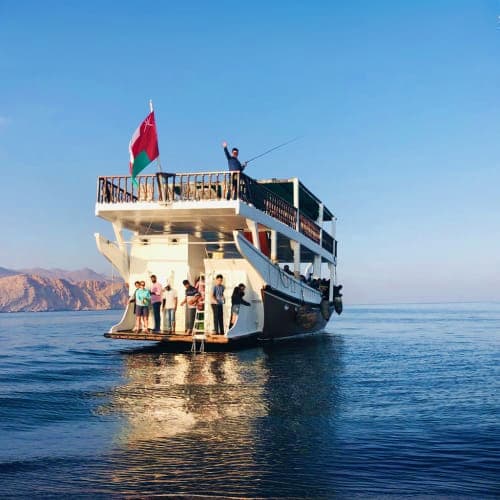 Ferry boat with Turkish flag anchored in clear blue water near rocky coastal cliffs during Musandam Dibba tour
