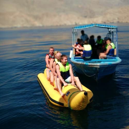 Group of tourists on yellow banana boat being towed by blue motorboat in calm blue sea waters during Musandam Dibba tour