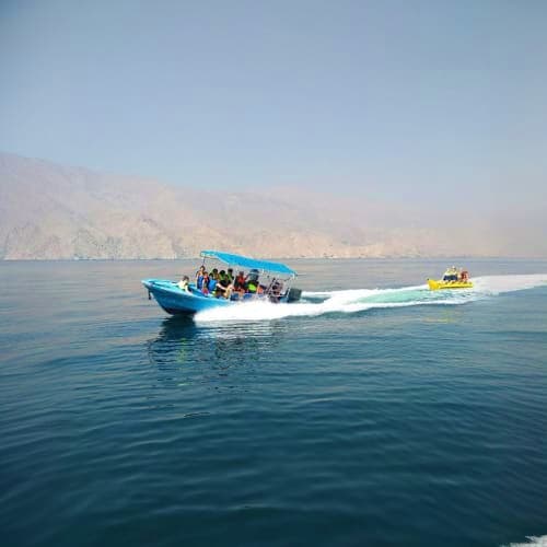 Musandam Dibba Tour Blue speedboat with passengers touring Musandam waters near coastal cliffs and rocky formations