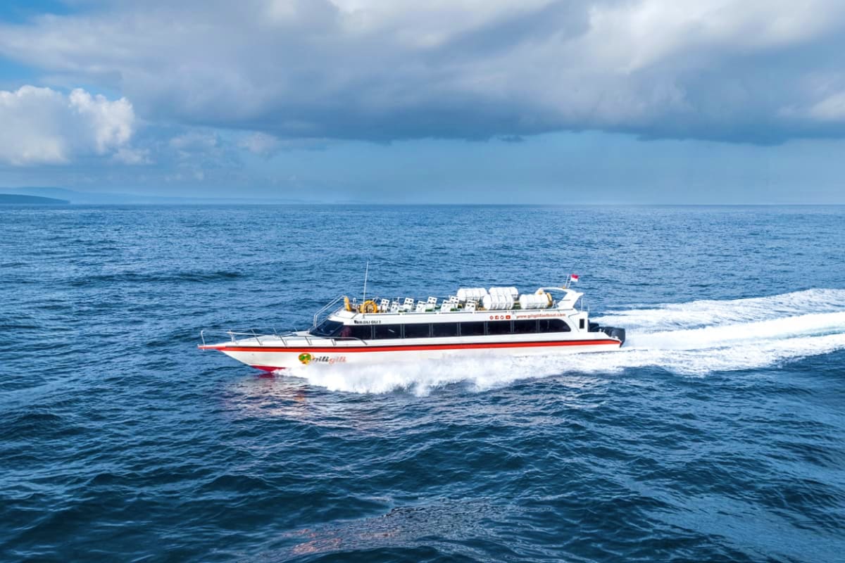 Nusa Penida Fast Boat Fast passenger ferry boat with red and white hull riding through ocean waves under cloudy sky