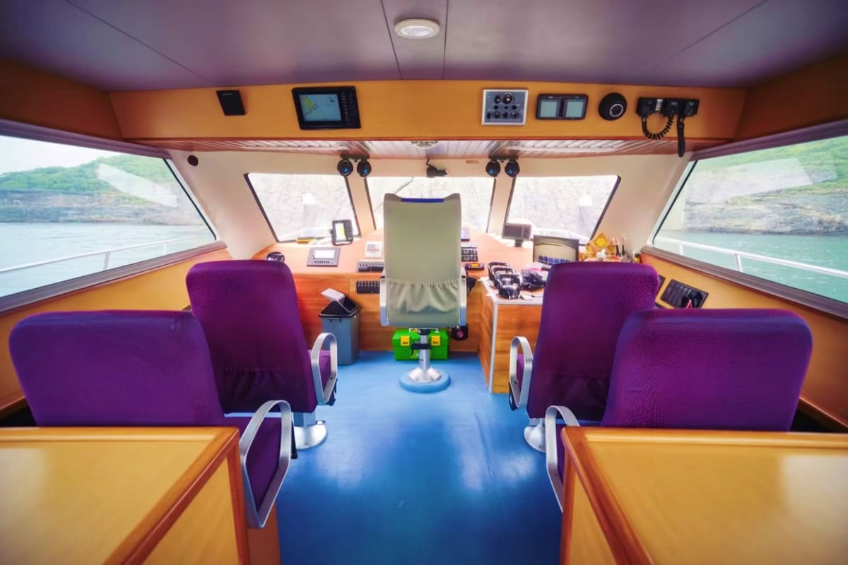 Nusa Penida Fast Boat Interior of Nusa Penida Fast Boat showing purple passenger seats, orange control panel with navigation equipment, and water v