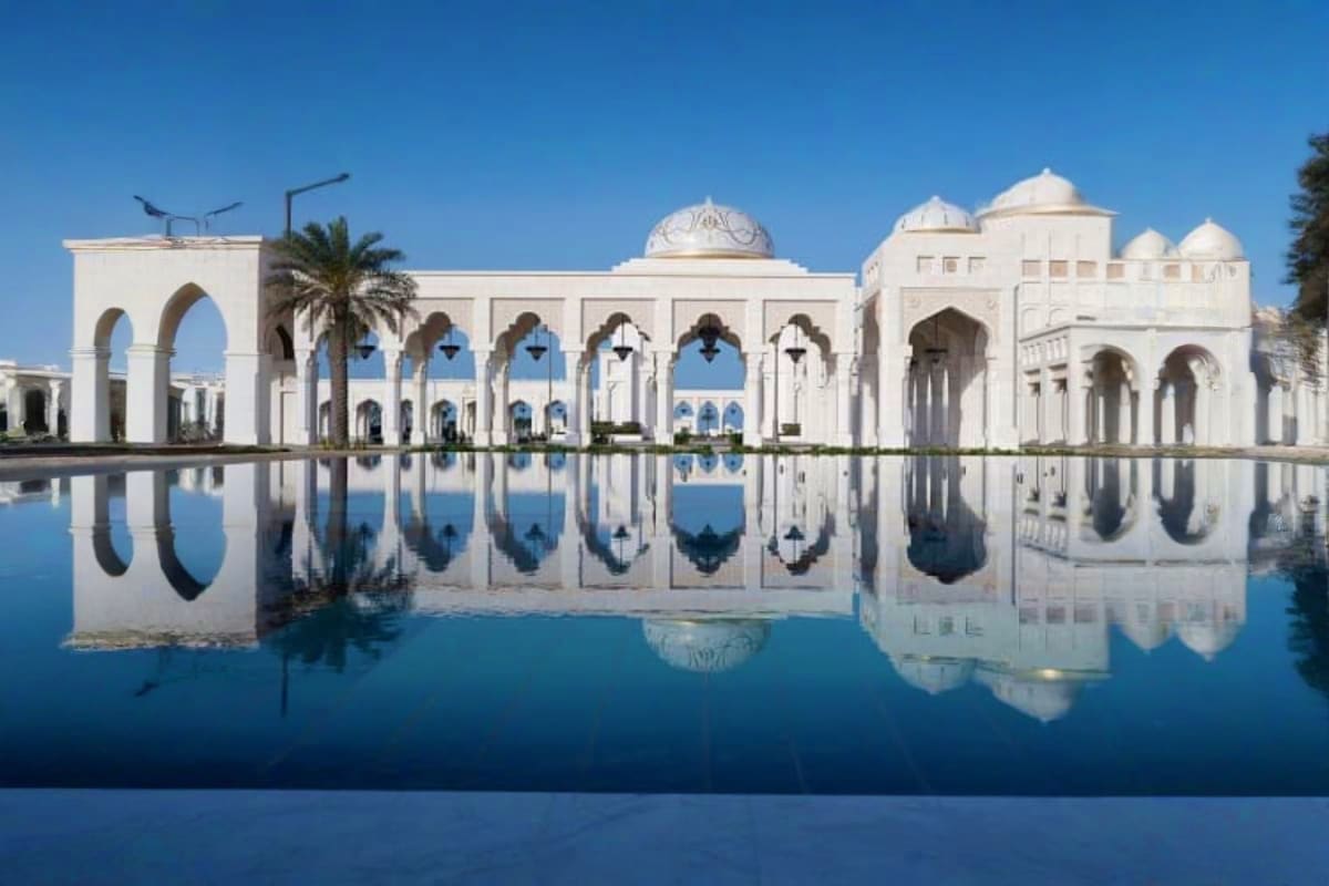 White palace with arched colonnades and domes reflected in still water pool under clear blue sky