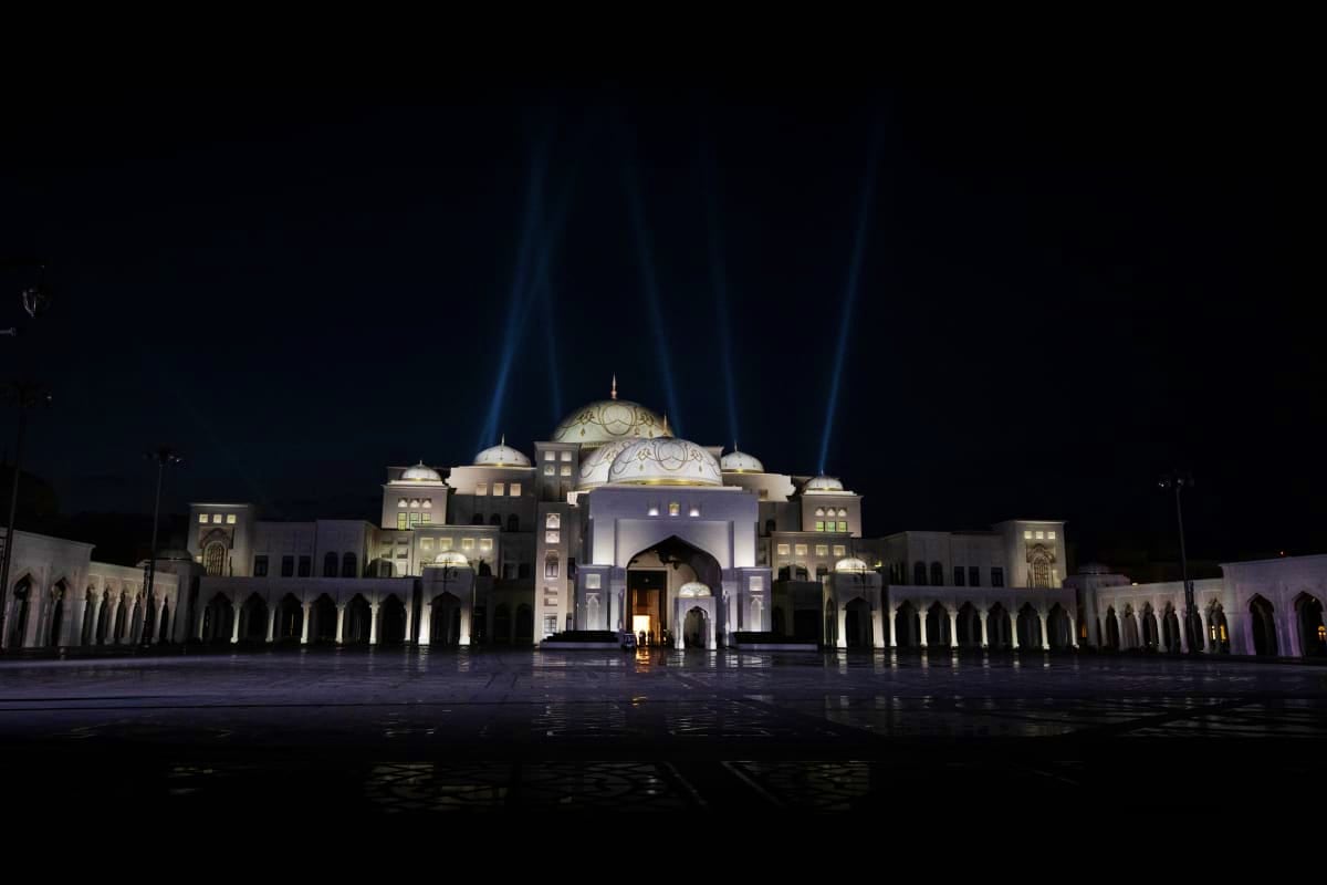 Qasr Al Watan palace illuminated at night with searchlight beams, featuring white stone architecture and reflecting pool in A