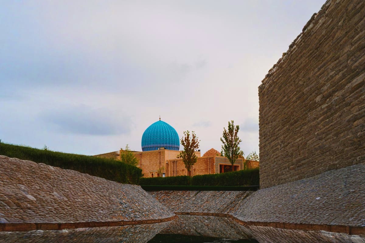 Blue-domed mosque with brick architecture viewed through stone fortress walls in Samarkand, Uzbekistan