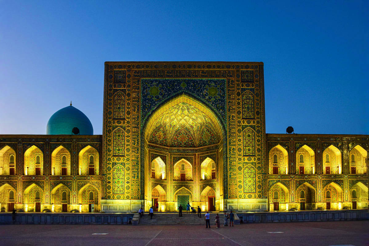 Illuminated Registan square with ornate tilework, golden archways, and turquoise dome at dusk in Samarkand, Uzbekistan