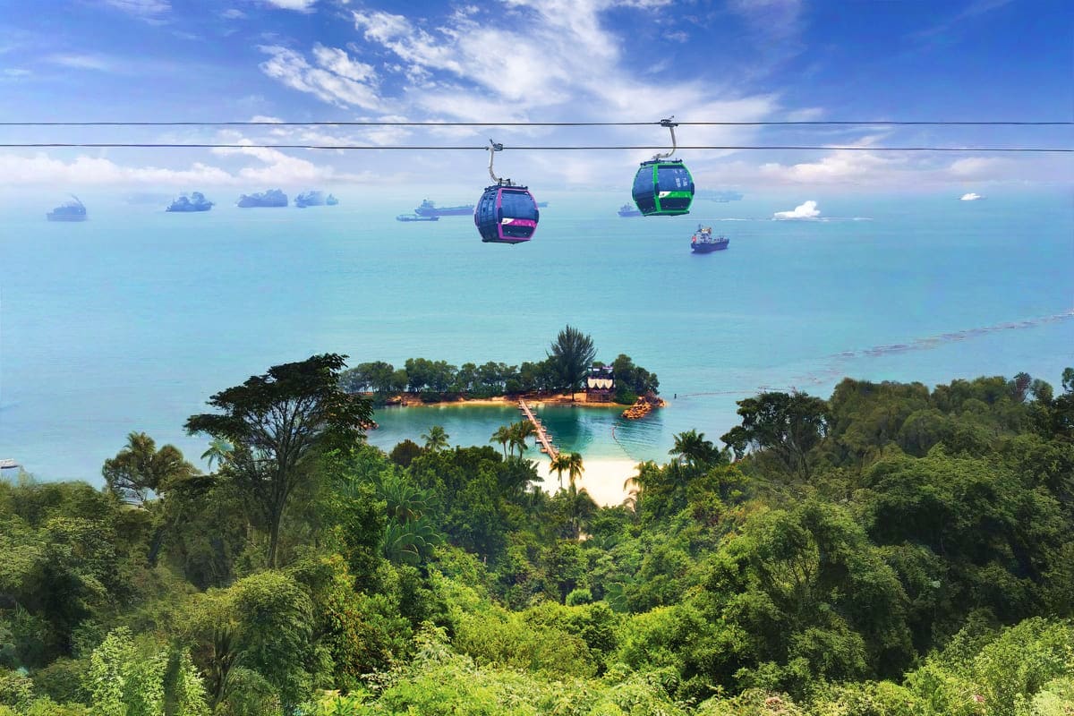 Sentosa Cable Car Ride Cable car pods suspended above tropical island with turquoise ocean, white sand beach, and lush green vegetation below