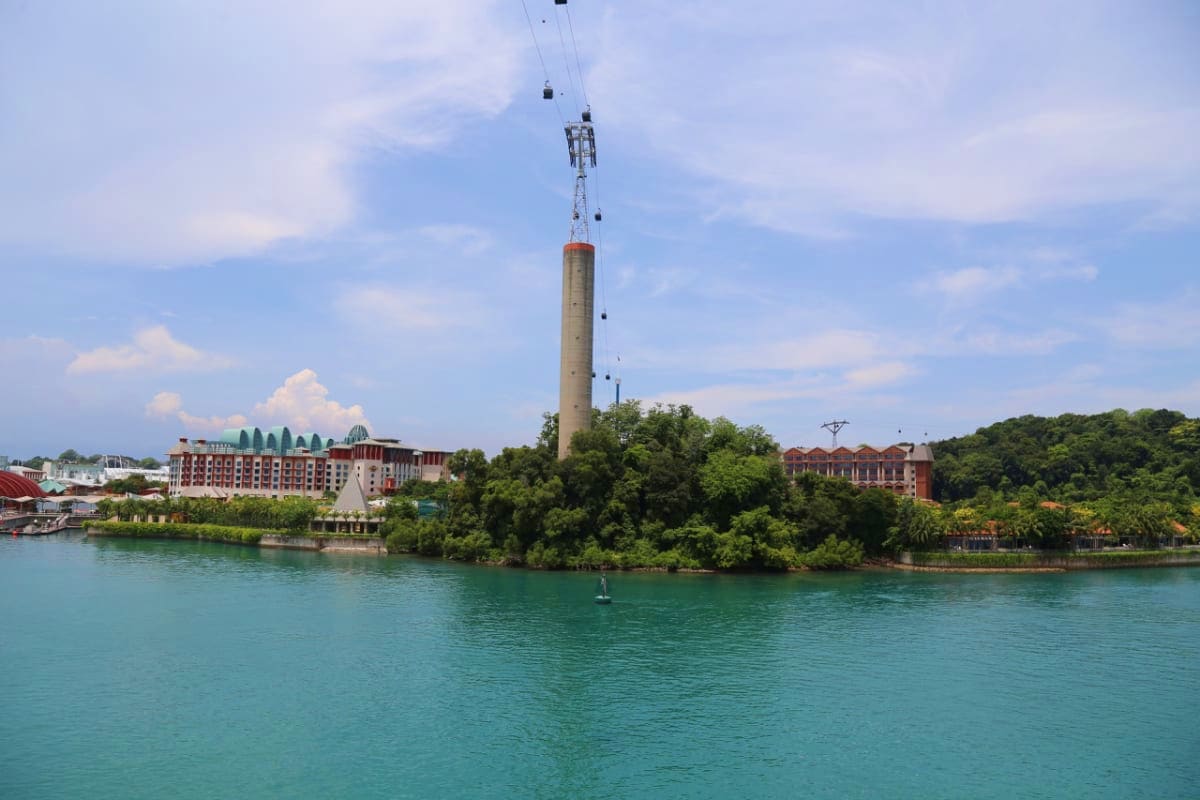Sentosa Cable Car tower rising above turquoise water with resort buildings and lush greenery on the island shore