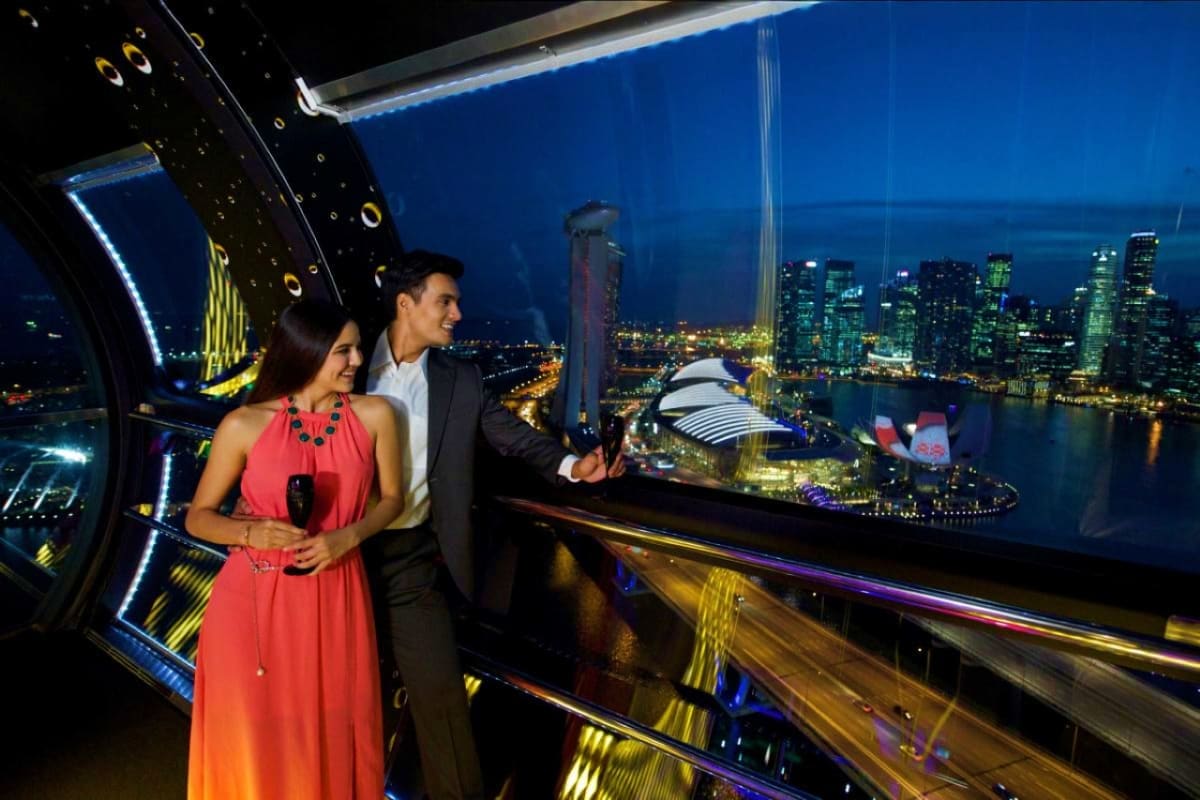 Couple enjoying nighttime city views from Singapore Flyer observation wheel overlooking illuminated downtown skyline