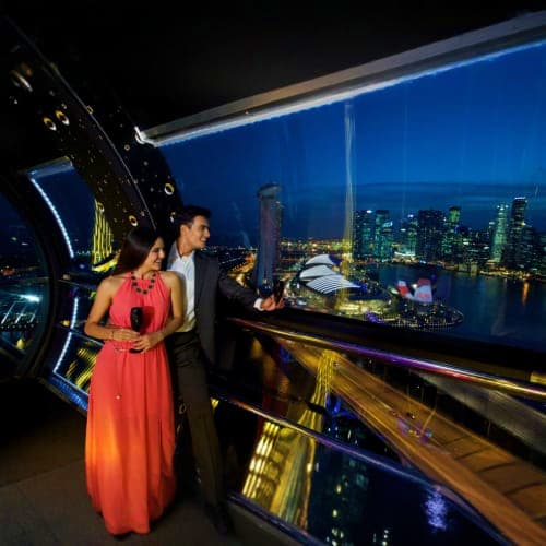 Couple in formal attire viewing Singapore skyline and Marina Bay from Singapore Flyer observation deck at night