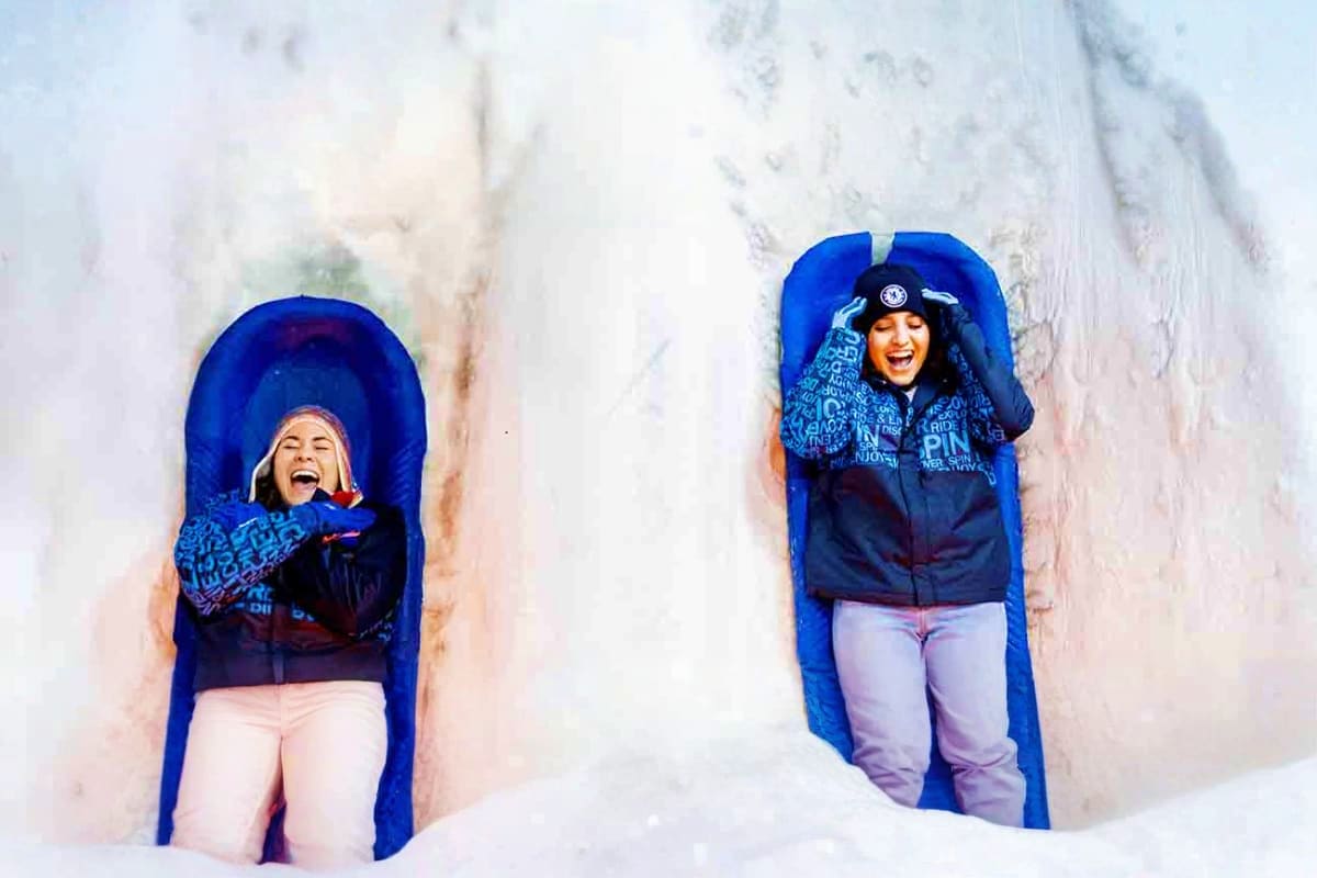 Two visitors sliding down an icy blue tube slide at Ski Dubai indoor snow park