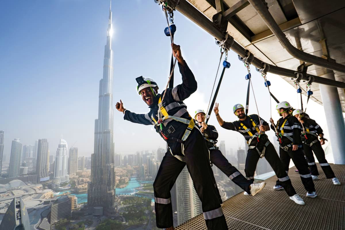Sky Views Edge Walk Group of people in safety harnesses performing edge walk on high-rise building platform with Burj Khalifa and Dubai skyline i