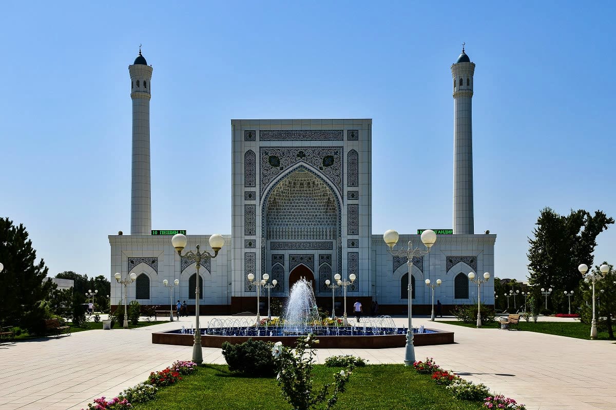 Tashkent City Tour White marble mosque with two minarets and central iwan, featuring fountain and manicured gardens in foreground under clear bl