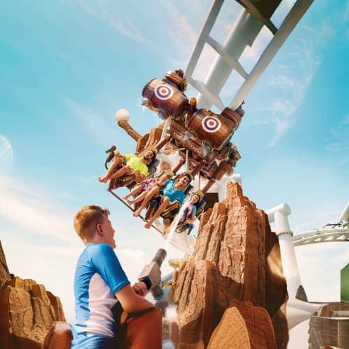 Visitors riding a spinning water ride at Yas Water World theme park with artificial rock formations and clear blue sky