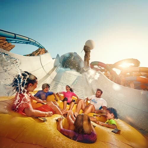 Group of visitors sliding down a water slide at Yas Water World theme park with splashing water and blue sky