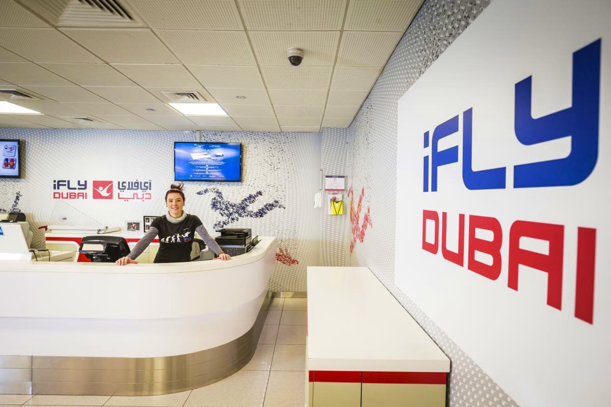 iFly Dubai iFly Dubai reception desk with staff member and blue signage in modern white interior space