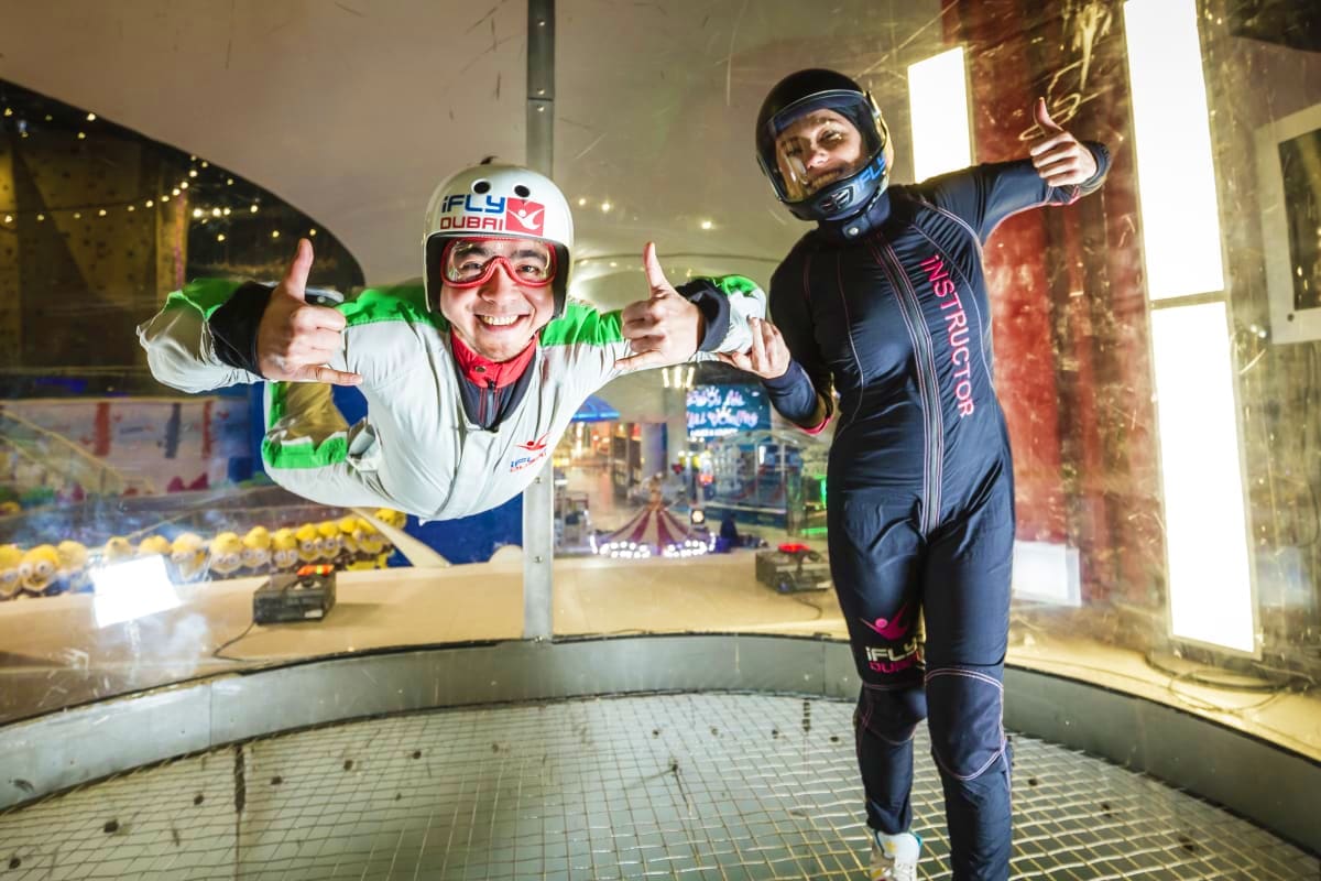 iFly Dubai Two people indoor skydiving at iFly Dubai, one in white suit giving thumbs up, one in black suit standing beside, in wind tun
