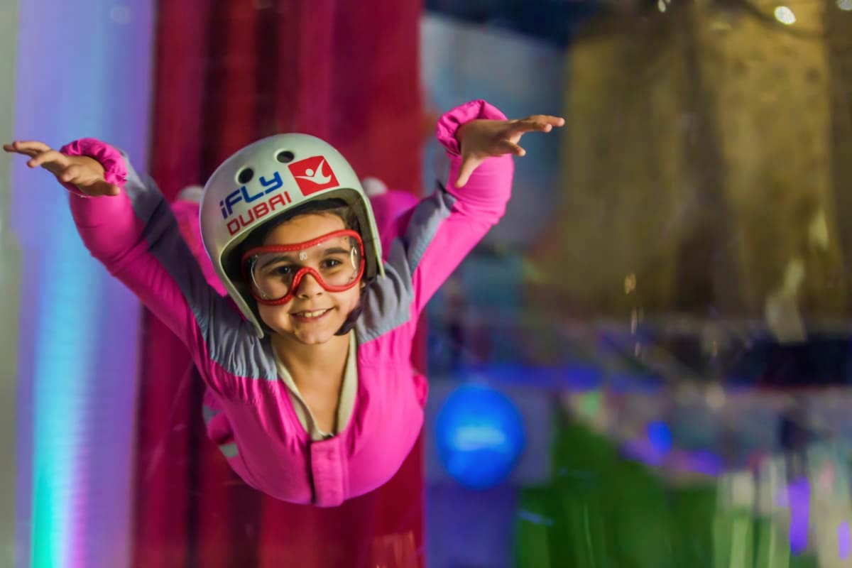 iFly Dubai Child in bright pink flight suit and white helmet enjoying indoor skydiving at iFly Dubai wind tunnel facility