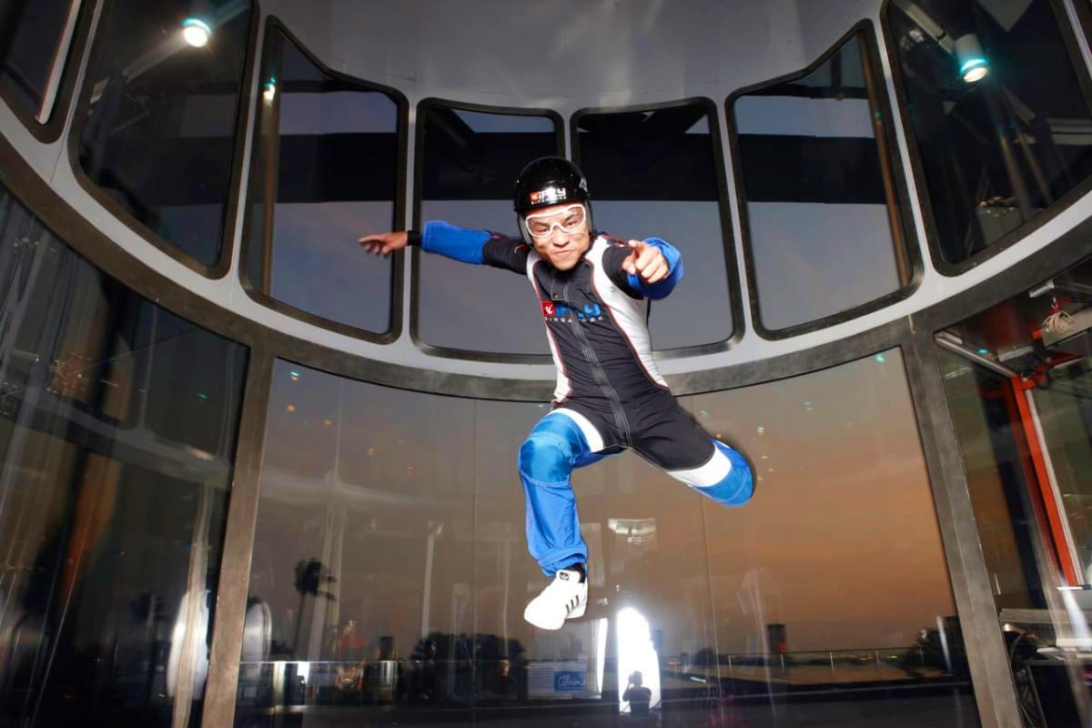iFly Singapore Person indoor skydiving in blue and black suit inside iFly wind tunnel facility with large windows