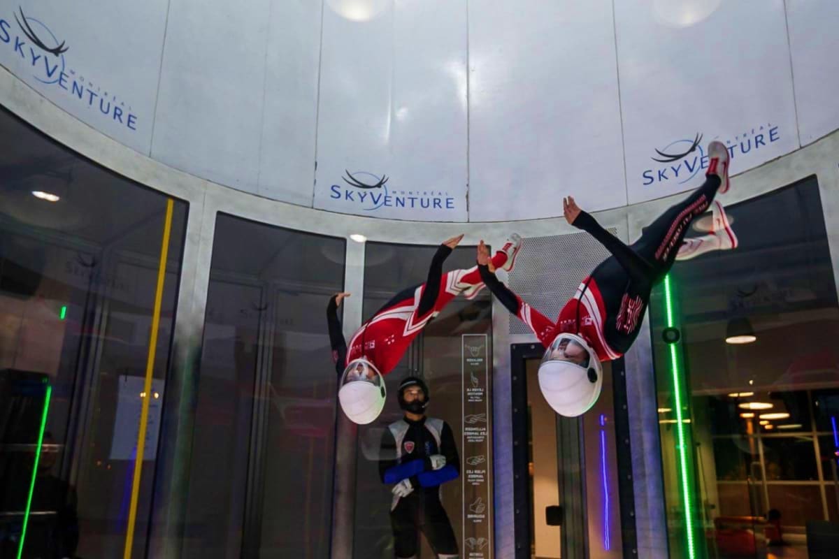iFly Singapore Two people indoor skydiving in a vertical wind tunnel at iFly Singapore with "Skyventure" branding visible on the walls