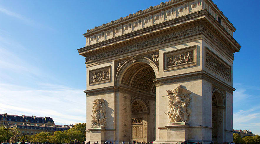 Arc de Triomphe monument in Paris with ornate stone carvings, sculptural reliefs, and classical arches against blue sky