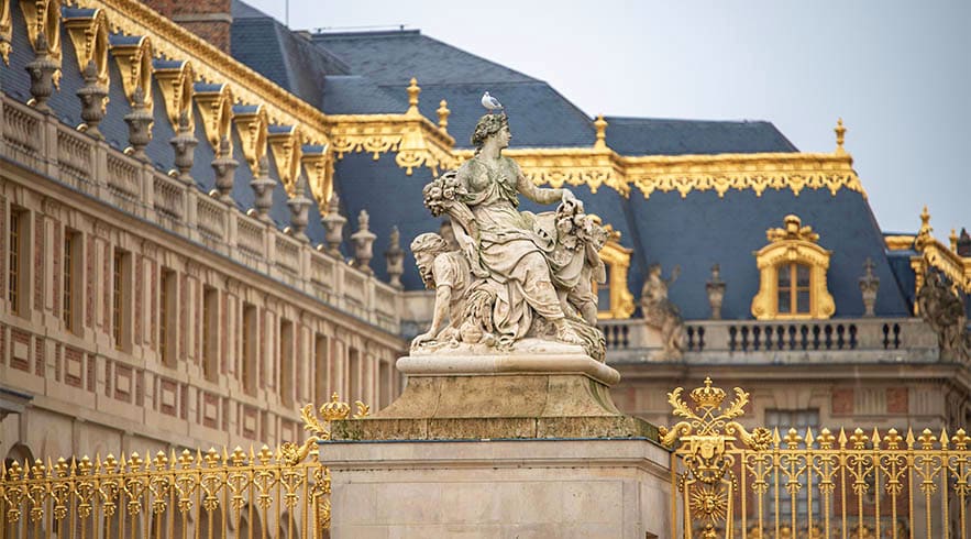 Marble statue with golden gates and ornate Palace of Versailles architecture in background