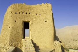 Ancient mud brick fortress with single entrance opening, set against desert landscape and clear blue sky in Ras Al Khaimah