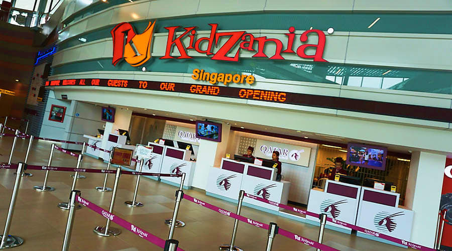 KidZania Singapore KidZania Singapore entrance with red logo sign and Qatar Airways branded ticket counters in indoor shopping mall setting