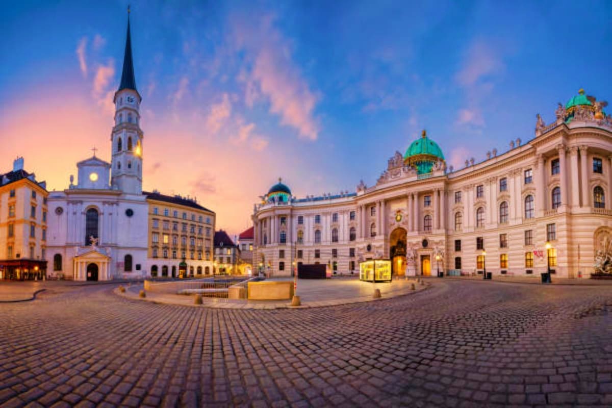 Michaelerplatz square in Vienna, Austria at dusk with illuminated historic buildings and church spire