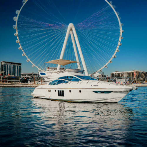 White luxury yacht anchored in Dubai waters with Ferris wheel in background under clear blue sky