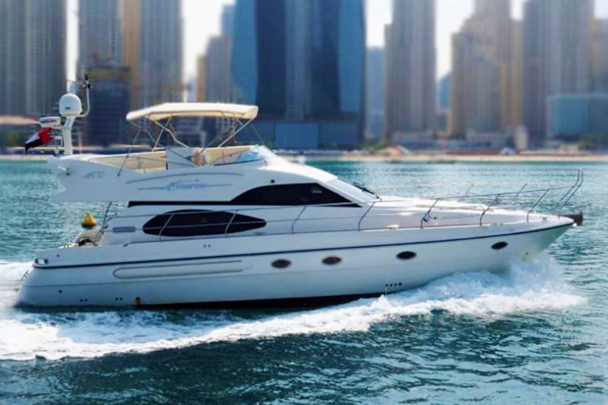 White luxury motor yacht anchored in shallow water with city skyline in background
