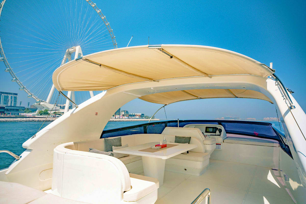 Maiora X12 yacht flybridge with retractable canopy, seating area, and Ferris wheel visible in background on blue water