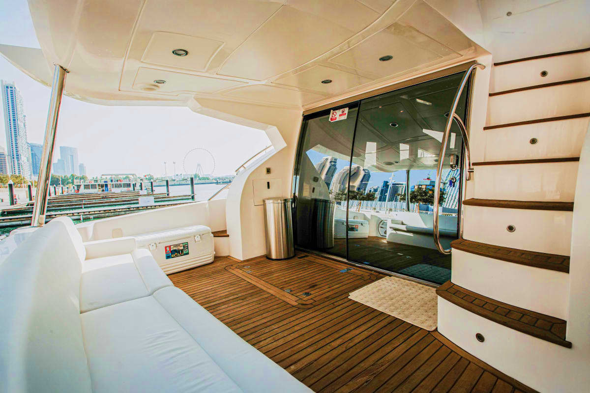 Spacious yacht deck with white seating, wooden flooring, and glass doors overlooking marina with city skyline and ferris whee