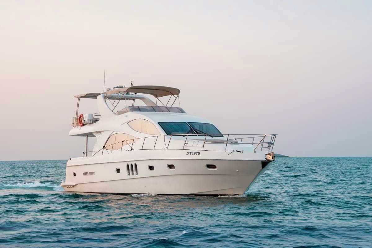 White luxury motor yacht anchored in calm turquoise ocean water with dark canopy top and registration number DT1976 visible o