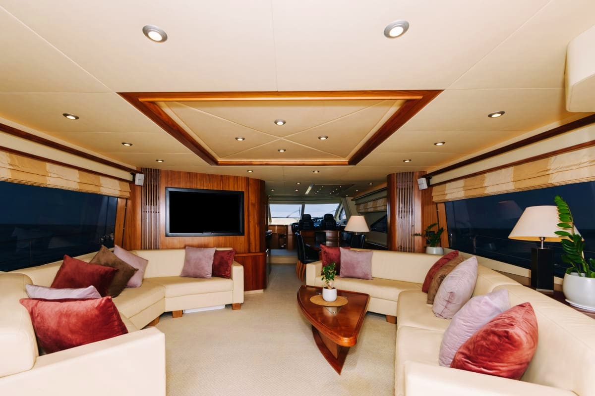 Luxury yacht interior salon with cream seating, wooden accents, flat-screen TV, and ocean views through windows
