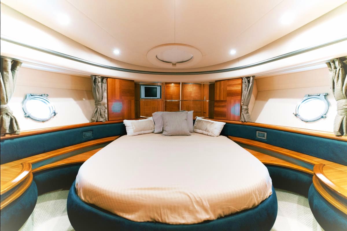 Luxury yacht master bedroom with round bed, wood paneling, porthole windows, and curved ceiling with recessed lighting