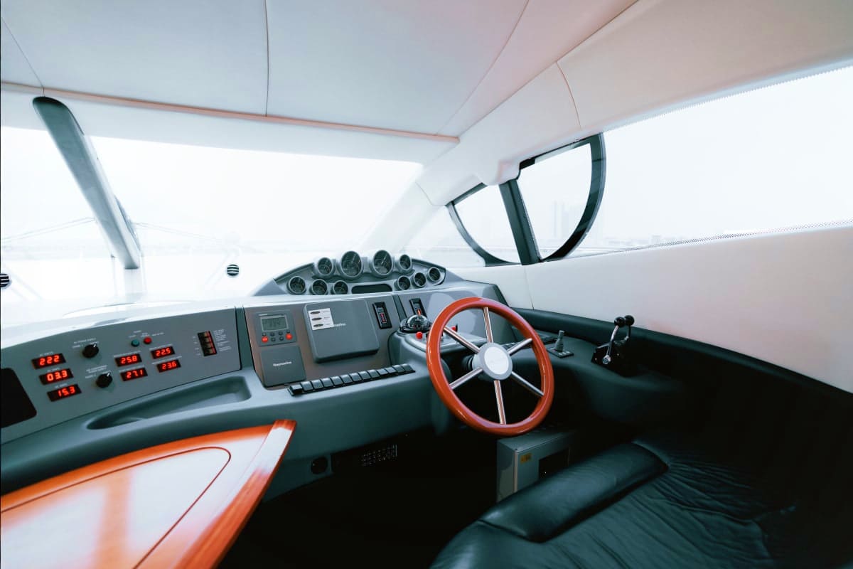 Interior pilot house of 50 Ft Grand Voyage Yacht with red steering wheel, control dashboard, and panoramic windows