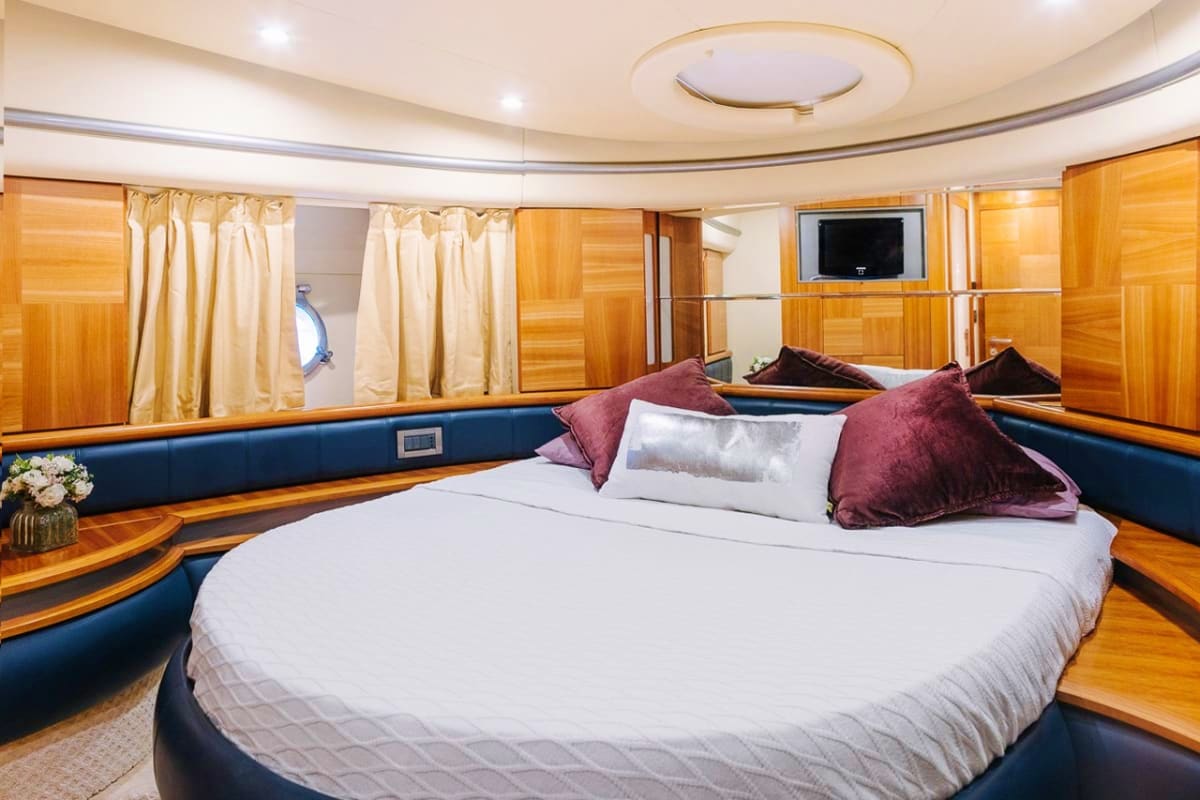 Luxury yacht master bedroom with round bed, burgundy pillows, wood paneling, blue upholstery, and TV mounted on wall