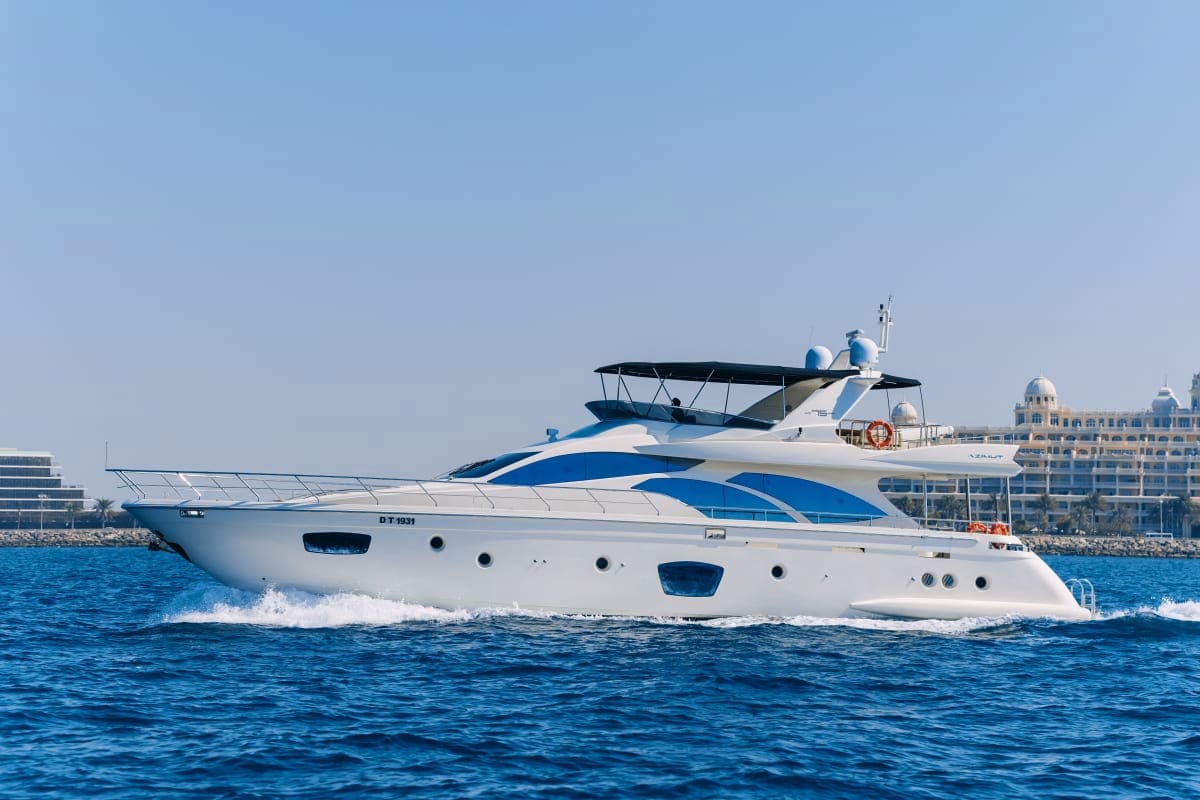75 Ft Supreme Luxury Yacht Luxury yacht with white hull and blue stripe cruising in clear blue water near coastal resort buildings