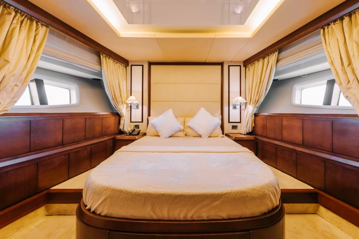75 Ft Supreme Luxury Yacht Luxurious yacht master bedroom with cream bedding, wooden paneling, gold curtains, and porthole windows on either side