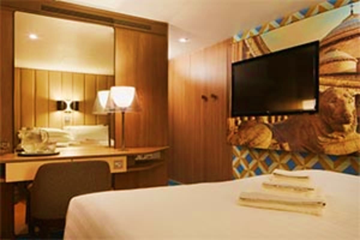 Costa Smeralda Mediterranean Spring Escape Cruise Luxury cruise ship cabin with wooden furnishings, large mirror, flat-screen TV, and white bedding