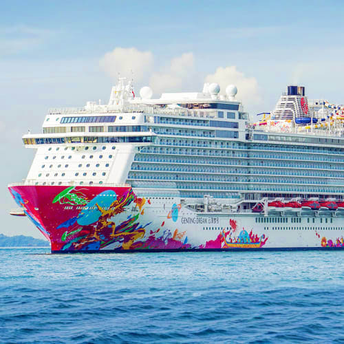 Genting Dream cruise ship with colorful pink and blue hull design sailing in blue ocean waters