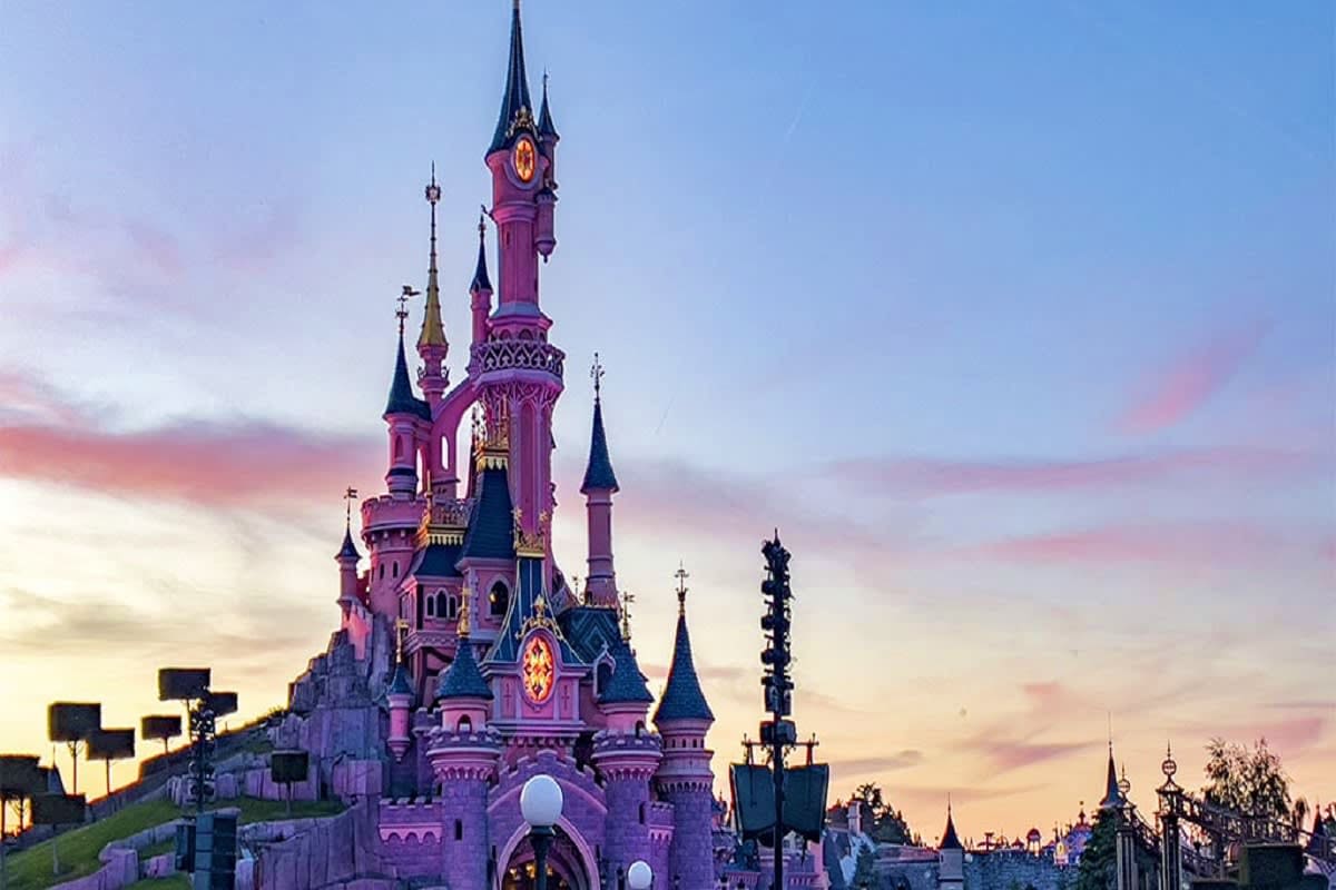 Cinderella's Castle at Disneyland Paris illuminated at dusk with pink and blue towers against a twilight sky