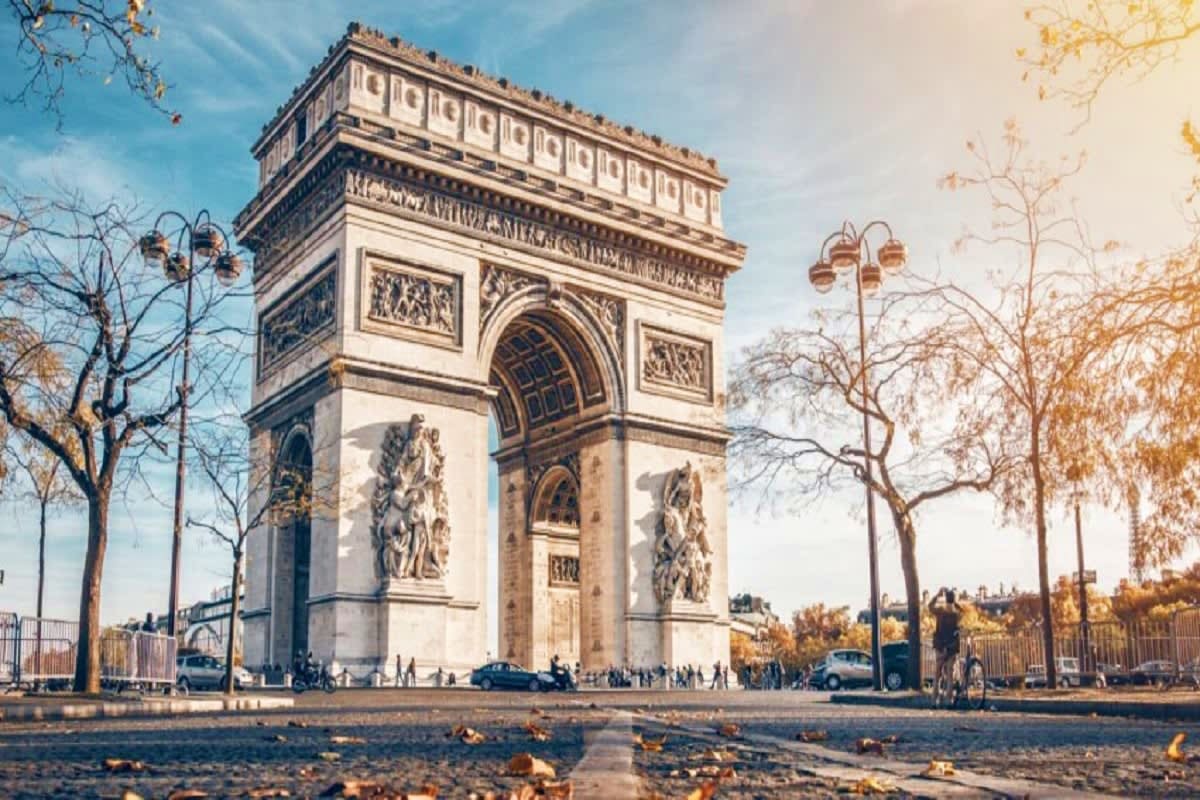Arc de Triomphe in Paris with autumn trees, street lamps, and tourists gathered around the iconic monument