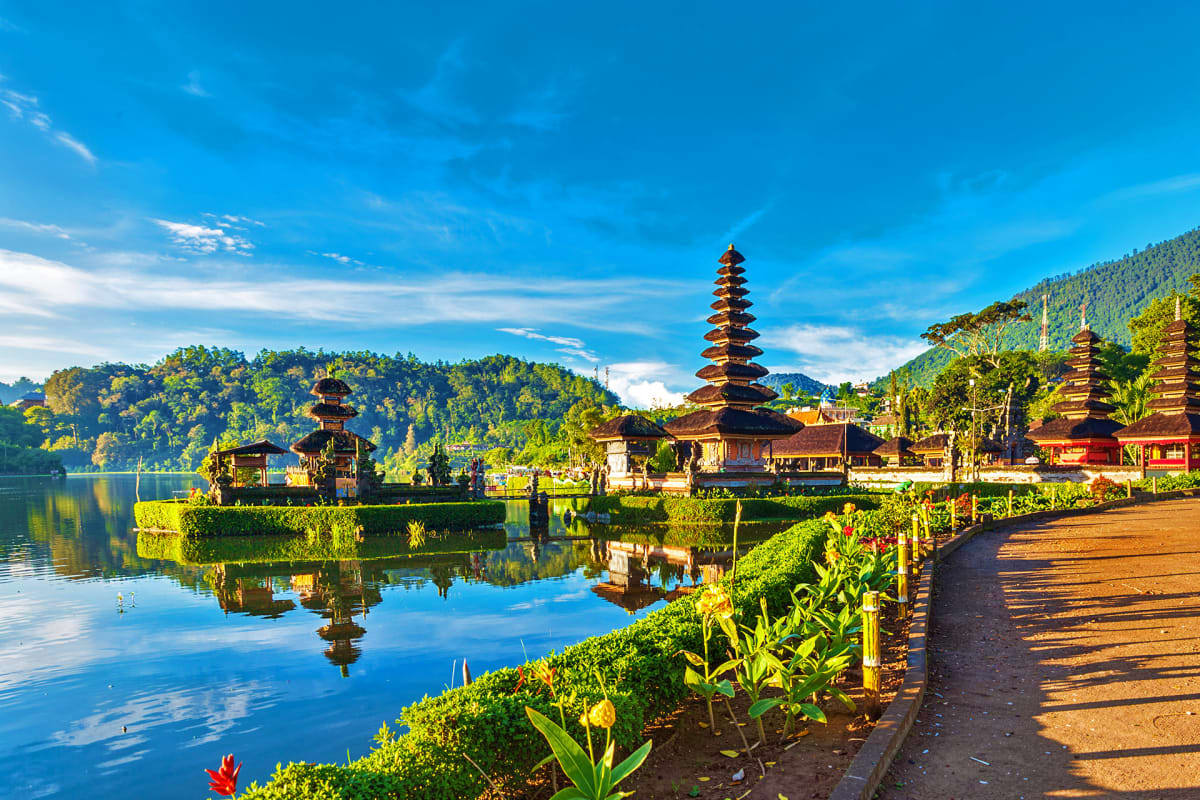 Pura Ulun Danu Bratan temple with tiered pagodas reflected in serene lake water, surrounded by lush green mountains and tropi