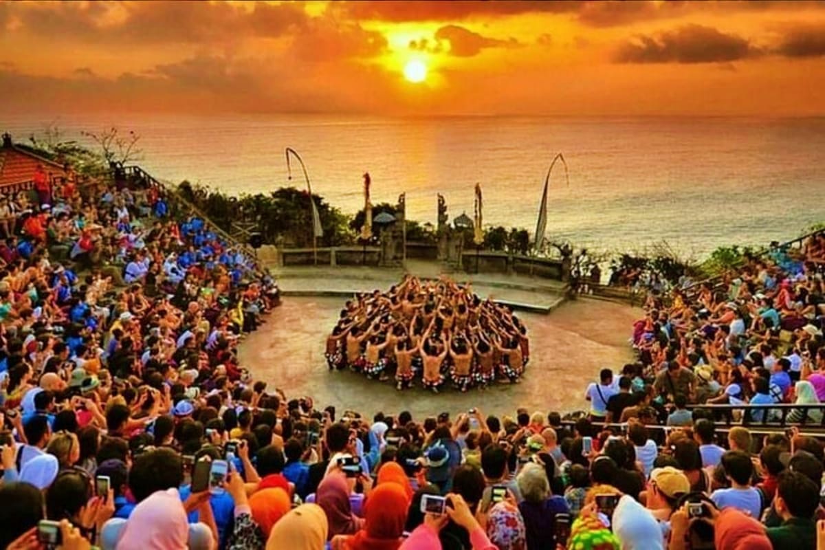 Traditional Balinese dance performance in circular formation surrounded by crowds of spectators at sunset overlooking the oce